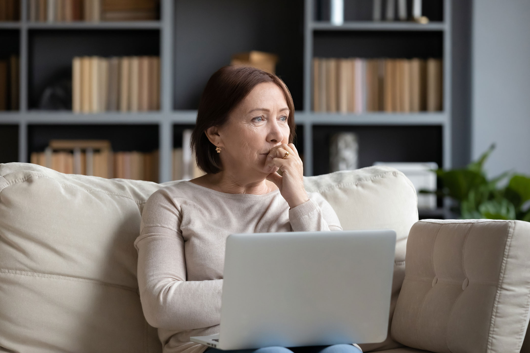 BHRT near me – Middle-aged woman sitting on a couch with a laptop, looking thoughtful and concerned, reflecting the impact of hormone imbalance