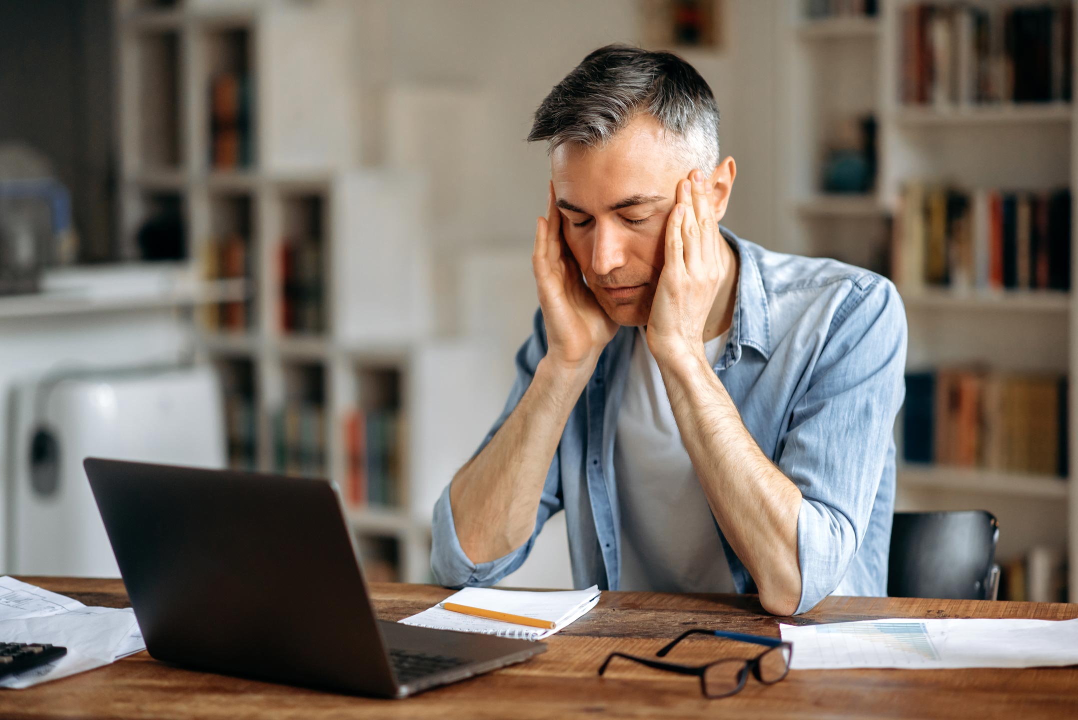 Tired middle-aged man sitting at desk with hands clasped, looking drained — low testosterone symptoms fatigue and brain fog in men